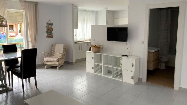 Un soggiorno moderno con zona pranzo, una TV a parete e cucina visibile attraverso un'apertura.