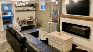 A modern living room with a sofa, a fireplace, a TV mounted above it, and a dining area in the background. - Stay at the Lazy Llama House with Self Check-In (Lincoln)