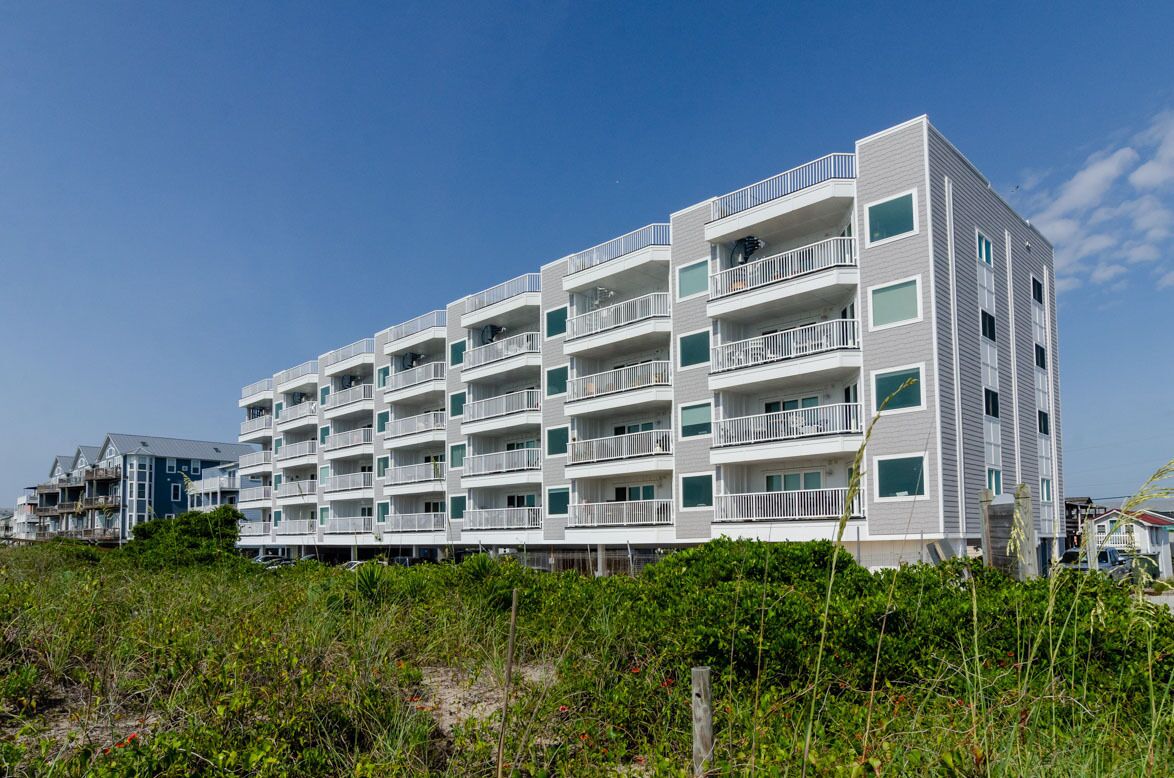 A multi-story hotel with balconies, located near a beach.