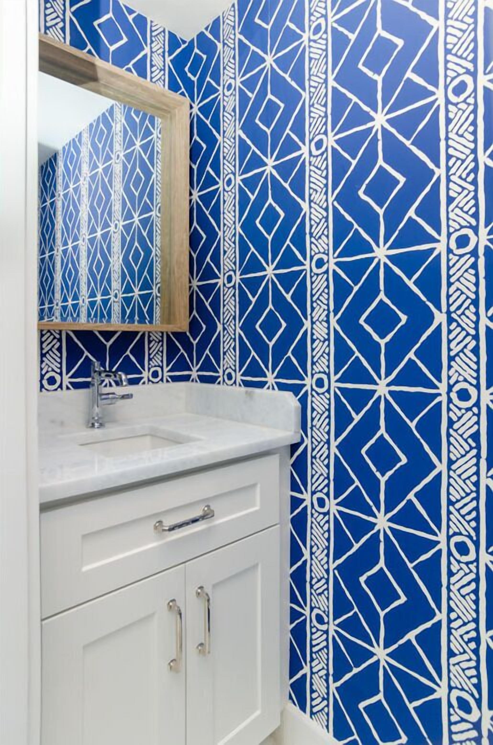 A bathroom with a white sink, a mirror, and a cabinet against a blue patterned wall.