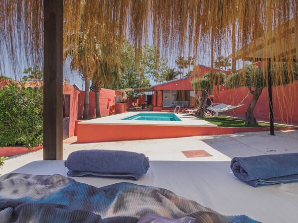 A swimming pool with lounge chairs and towels, surrounded by a red fence and palm trees.