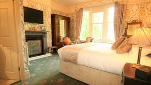 A bedroom with a large bed, a fireplace, a television mounted on the wall, and a window with curtains. - Kingscroft (Buxton)
