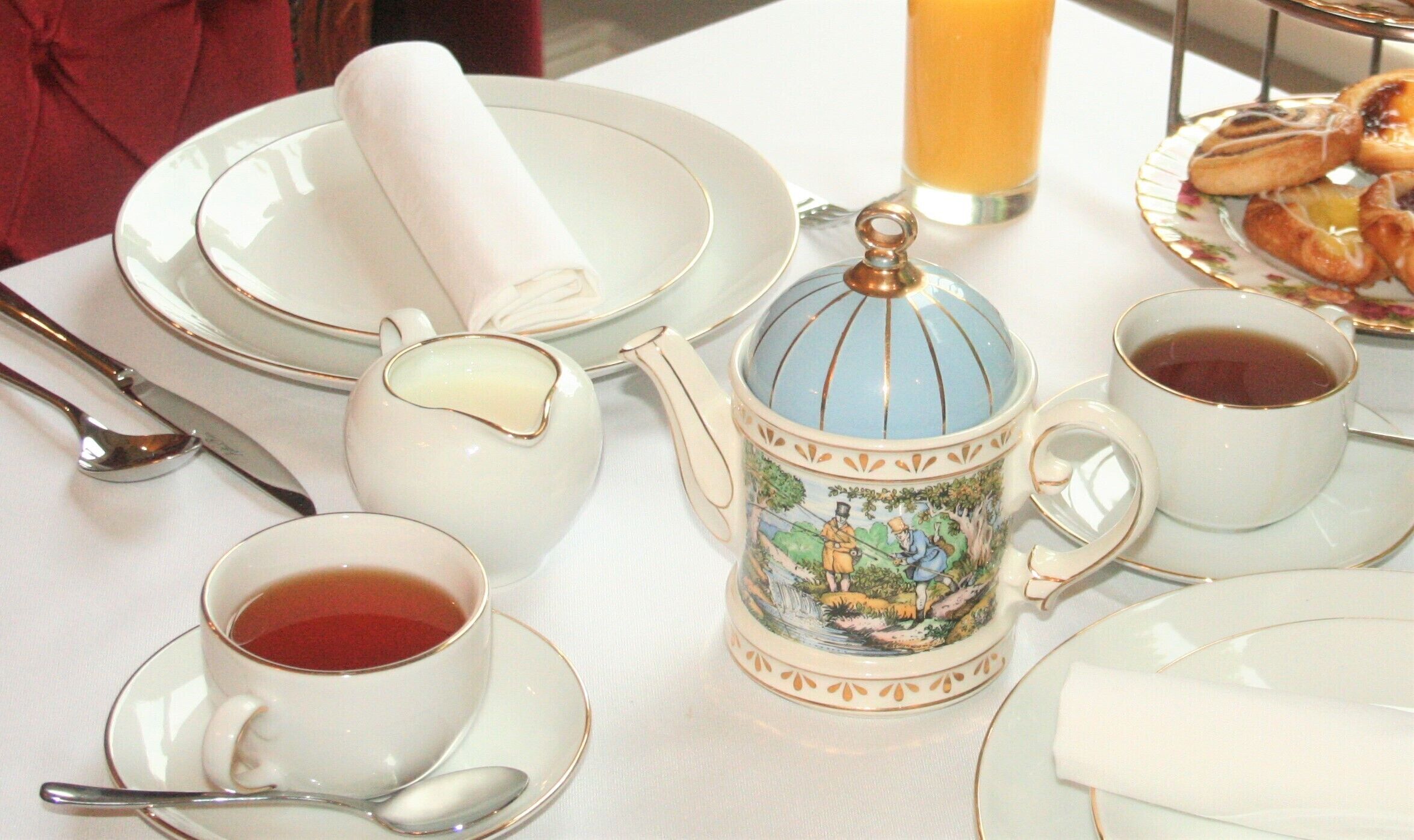 Una mesa dispuesta con platos blancos, una tetera, tazas, una jarra y una tacita de té.