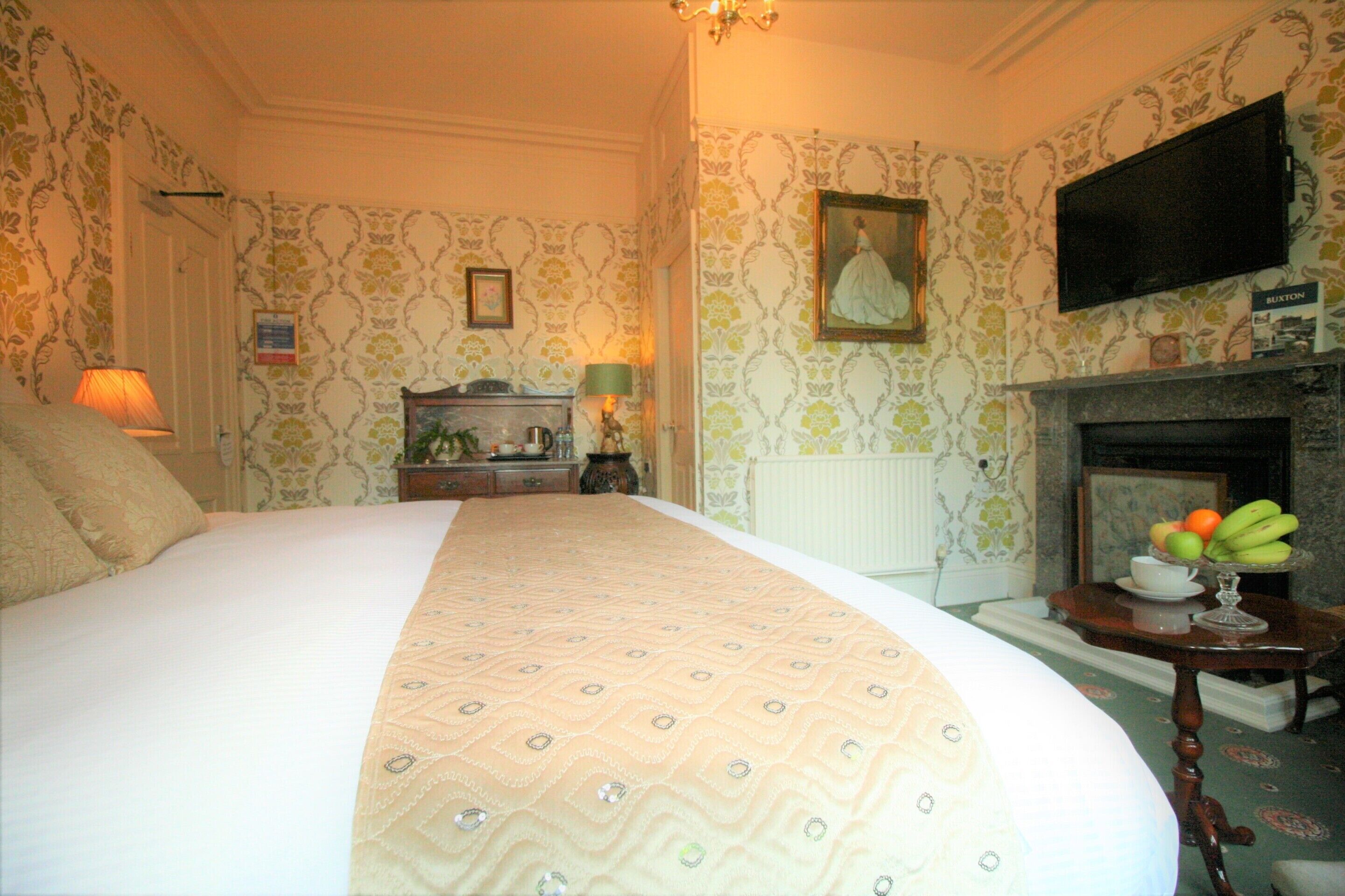 A hotel room with a large bed, a fireplace, a television, and a small table with fruit.