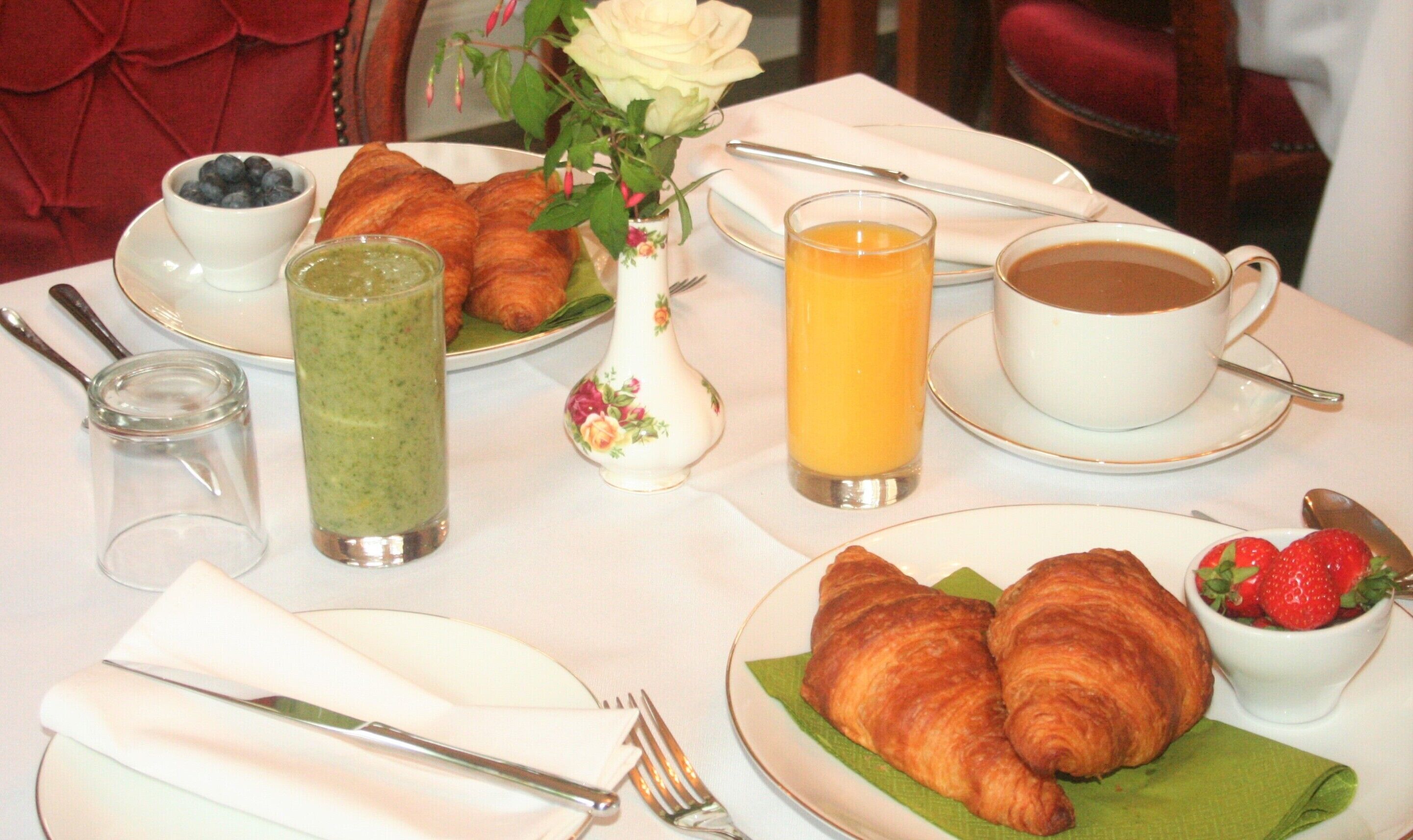 Desayuno con cruasanes, un batido verde, jugo de naranja, café y un tazón de fresas.