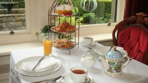 A breakfast setup with croissants, fruit, and coffee on a table by a window with a view of a garden. - Kingscroft (Buxton)