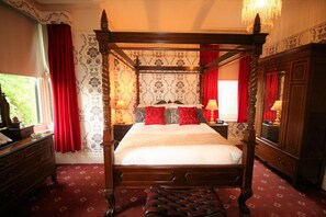 Una cama con dosel de madera, papel tapiz con estampado rojo y gris, y suelo cubierto de alfombra roja.