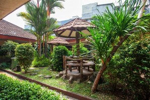 Un jardin agrémenté d’un kiosque en bois, de palmiers et d’un banc en pierre.