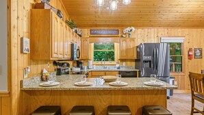 A wooden cabin kitchen with granite countertops, stainless steel appliances, and a central island with bar stools. - Gatlinburg cabin, 3 bed 2 bath, hot tub, no scary roads, PERFECT location (Gatlinburg)