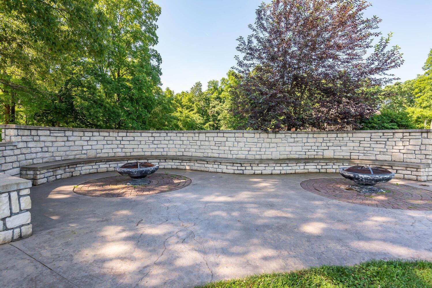 Un mur de pierre incurvé agrémenté de deux éléments décoratifs circulaires avec de l’eau et d’une zone dallée.