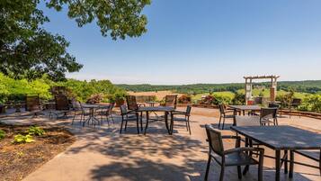 Un patio al aire libre con mesas y sillas, rodeado de vegetación y vistas a colinas ondulantes.