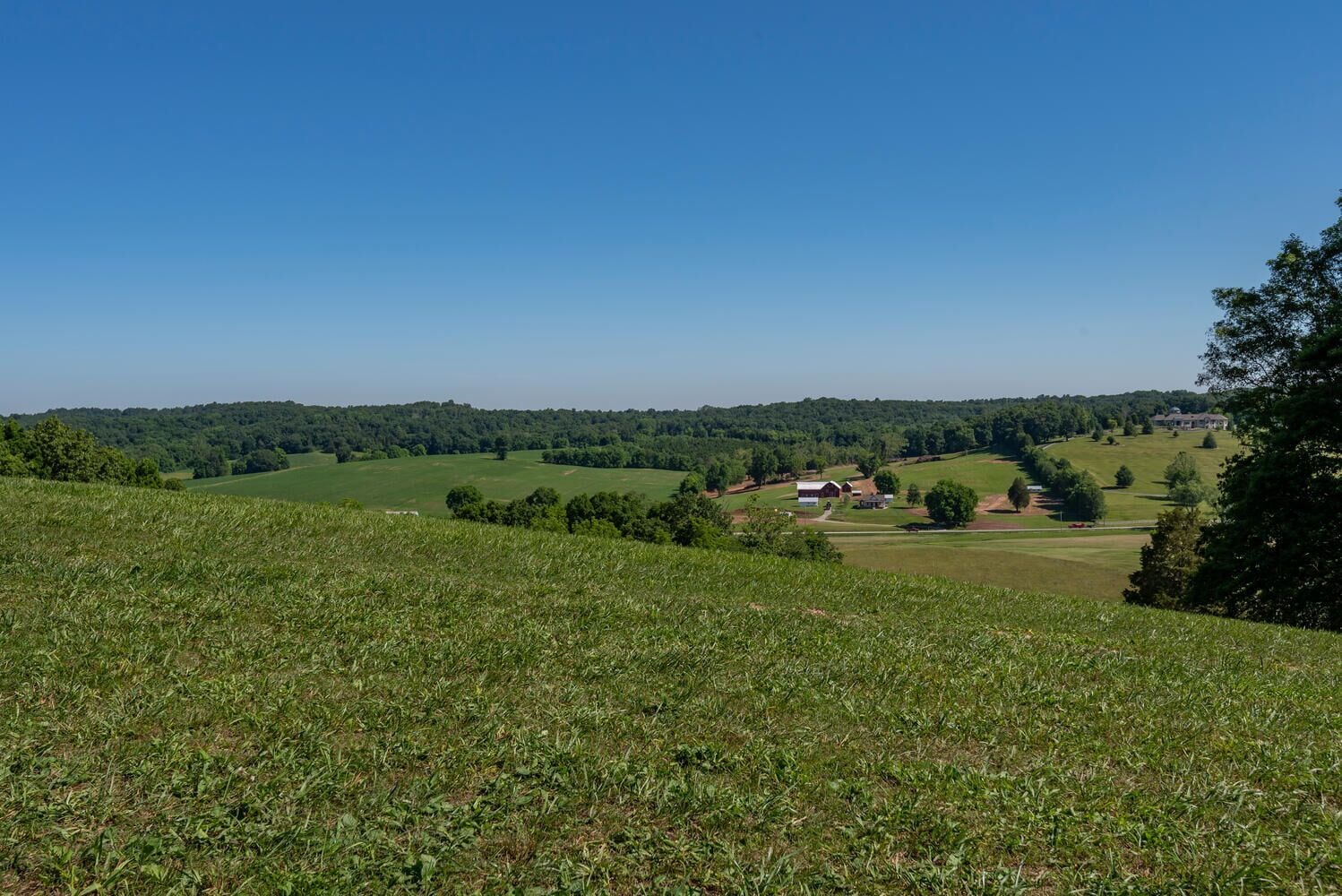 A rural landscape with rolling hills, scattered trees, and a few buildings, including a barn and a house.