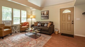 A living room with a sofa, armchairs, a coffee table, and a rug. There are windows with blinds, a lamp, and a door. - Beautiful New Cottage w/ Endless Hilltop Views (Paoli)