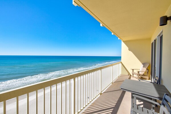 A balcony with a view of the ocean, a table, and two chairs.