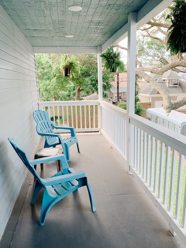 Een overdekte veranda met blauwe plastic stoelen en een witte balustrade.