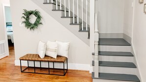 Un escalier avec des rampes blanches et des marches sombres, un banc avec des coussins et une guirlande décorative accrochée au mur.