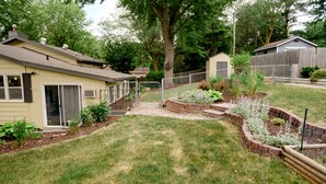 A residential backyard with a lawn, raised garden beds, a wooden fence, and a house with a garage. - Centrally located, spacious, updated home with room to Entertain! (Sioux Falls)