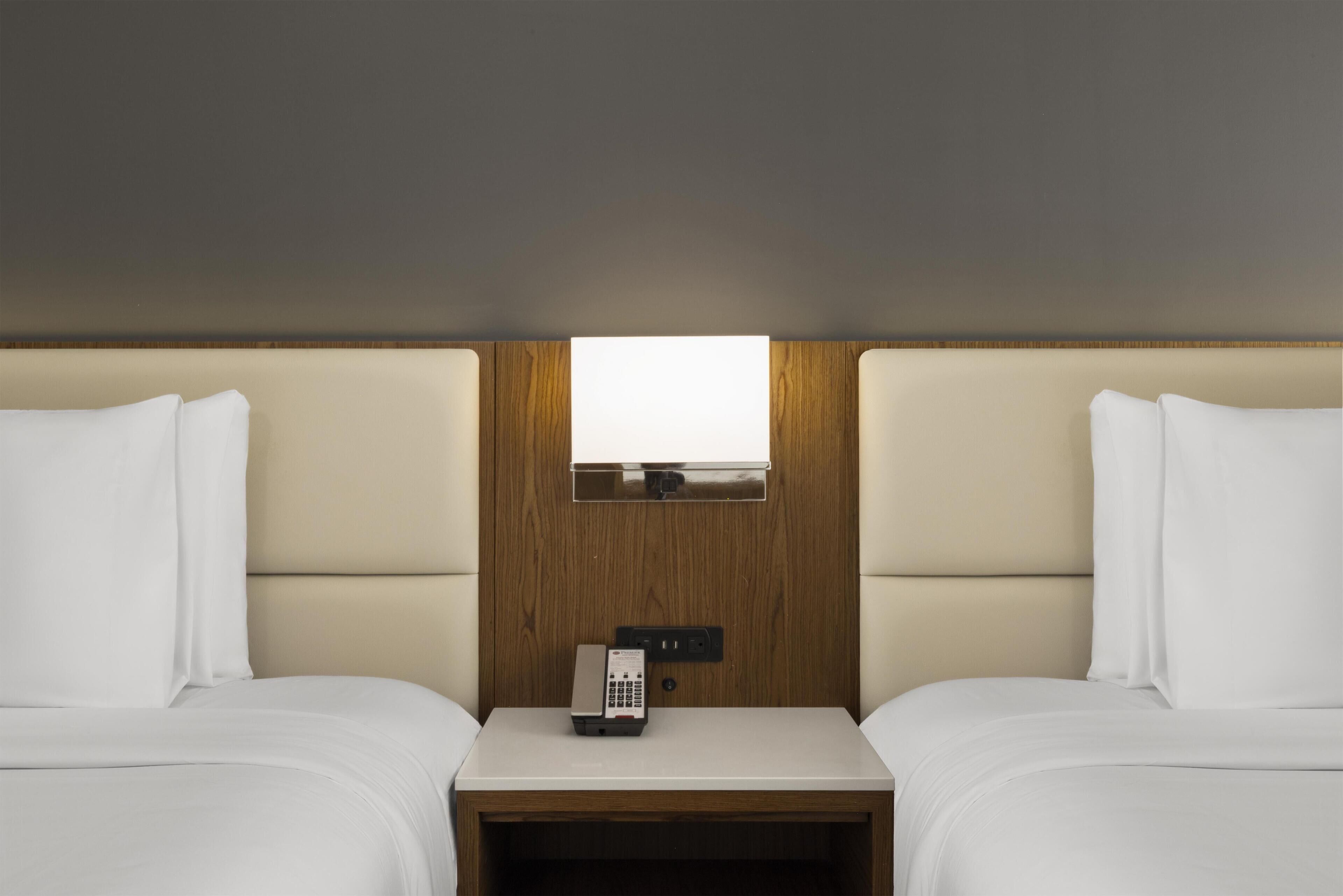 A hotel room with two beds, a wooden headboard, a small table with a phone, and a window.