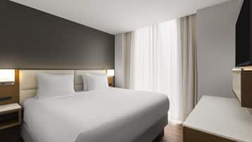 A modern hotel room with a large bed, a bedside table, a TV, and a window with curtains.
