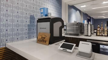 Un angolo caffè con una confezione di caffè a marchio, una macchina per caffè, un tablet e un terminale di pagamento.