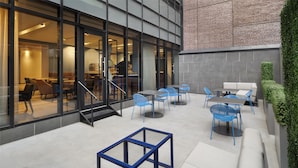 Een terras met tafels en stoelen, een glazen wand en een trap naar een binnenruimte.