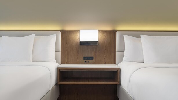 Een hotelkamer met twee bedden, een houten hoofdbord, een klein plankje en een lamp boven het bed.