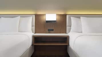 Una habitación de hotel con dos camas, un cabecero de madera, un estante pequeño y una lámpara sobre la cama.