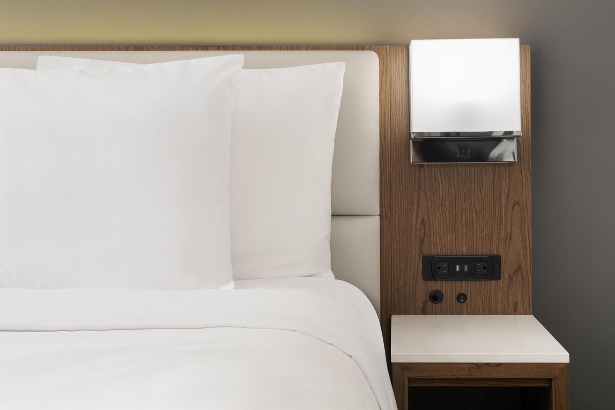 Un lit bien fait, avec du linge de lit blanc, une tête de lit en bois et une petite table de chevet à la surface blanche.