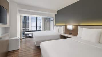Quarto de hotel com duas camas, televisão, escrivaninha e uma grande janela com vista para prédios.