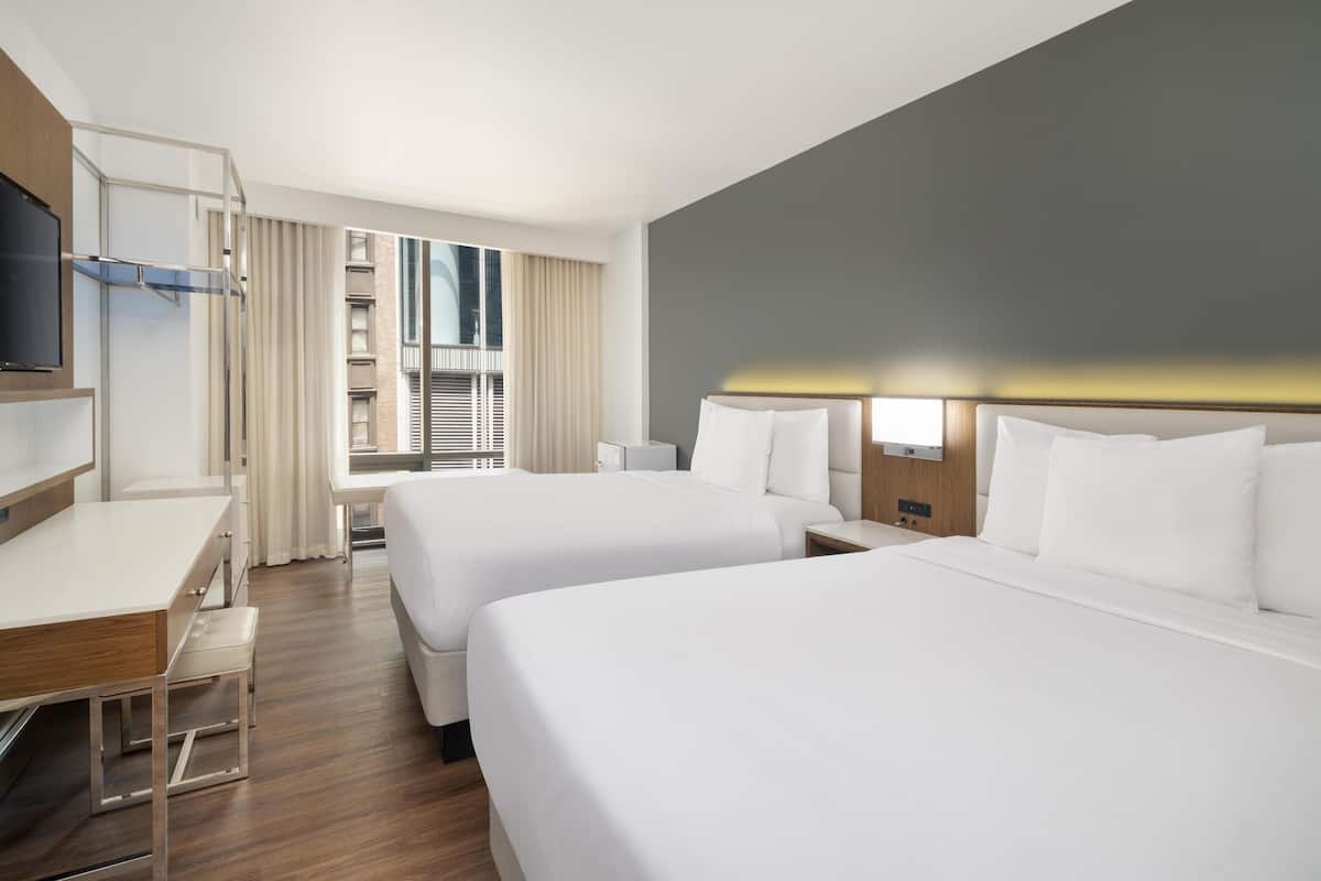 Ein Hotelzimmer mit zwei Betten, einem Schreibtisch, einem Fernseher und einem Fenster mit Vorhängen.