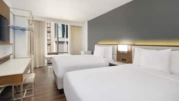 Quarto de hotel com duas camas, uma escrivaninha, uma TV e uma janela com cortinas.