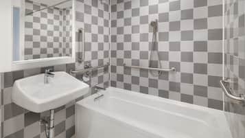 Un baño moderno con salpicadero de azulejos a cuadros, un lavabo blanco, una bañera y barras de apoyo.