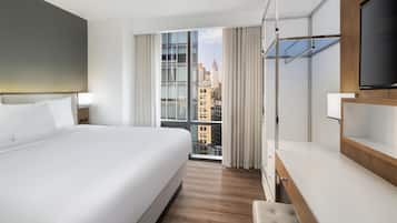 Habitación de hotel con una cama grande, televisión, escritorio y vistas a la ciudad.