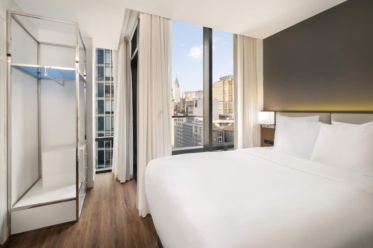 Ein Hotelzimmer mit einem großen Bett, einem begehbaren Kleiderschrank und Blick auf die Stadt.