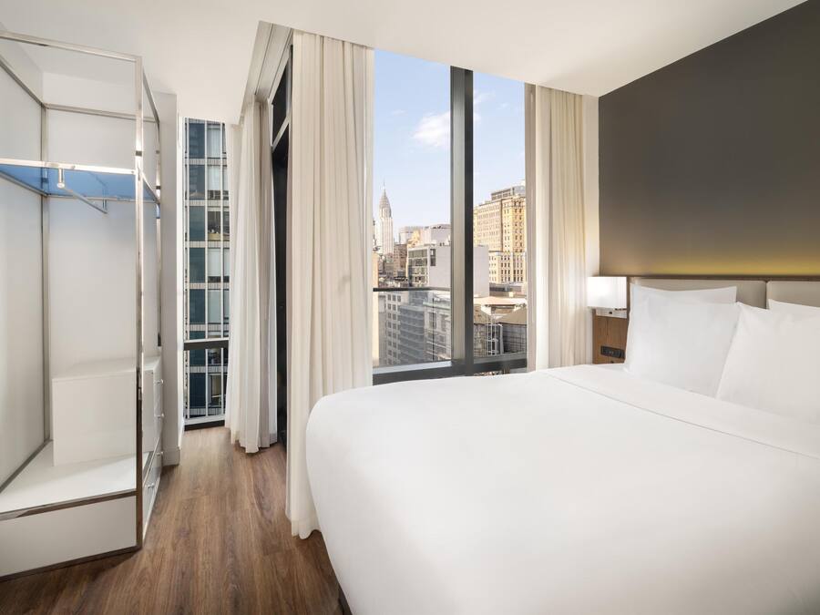 Habitación de hotel con una cama grande, vestidor y vista a la ciudad desde la ventana.