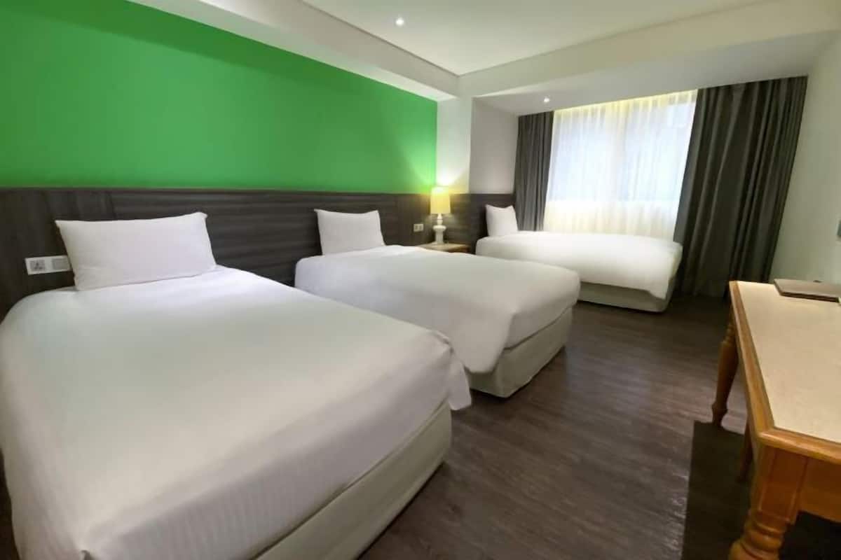 A hotel room with two beds, a desk, and a green accent wall.