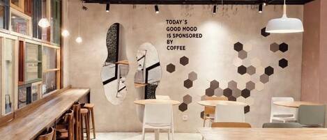 Interior de una cafetería con mesas, sillas, un reloj de pared y un diseño de pared con patrón hexagonal.