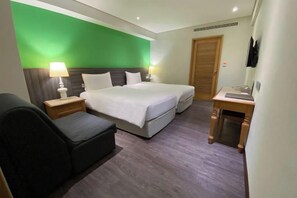 Una habitación de hotel con una cama, un escritorio, una silla y una pared verde decorativa.