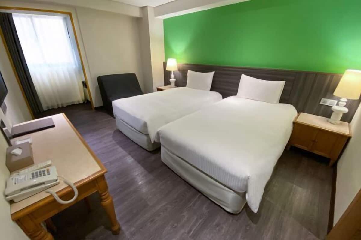 A hotel room with two beds, a desk with a telephone, and a green wall.