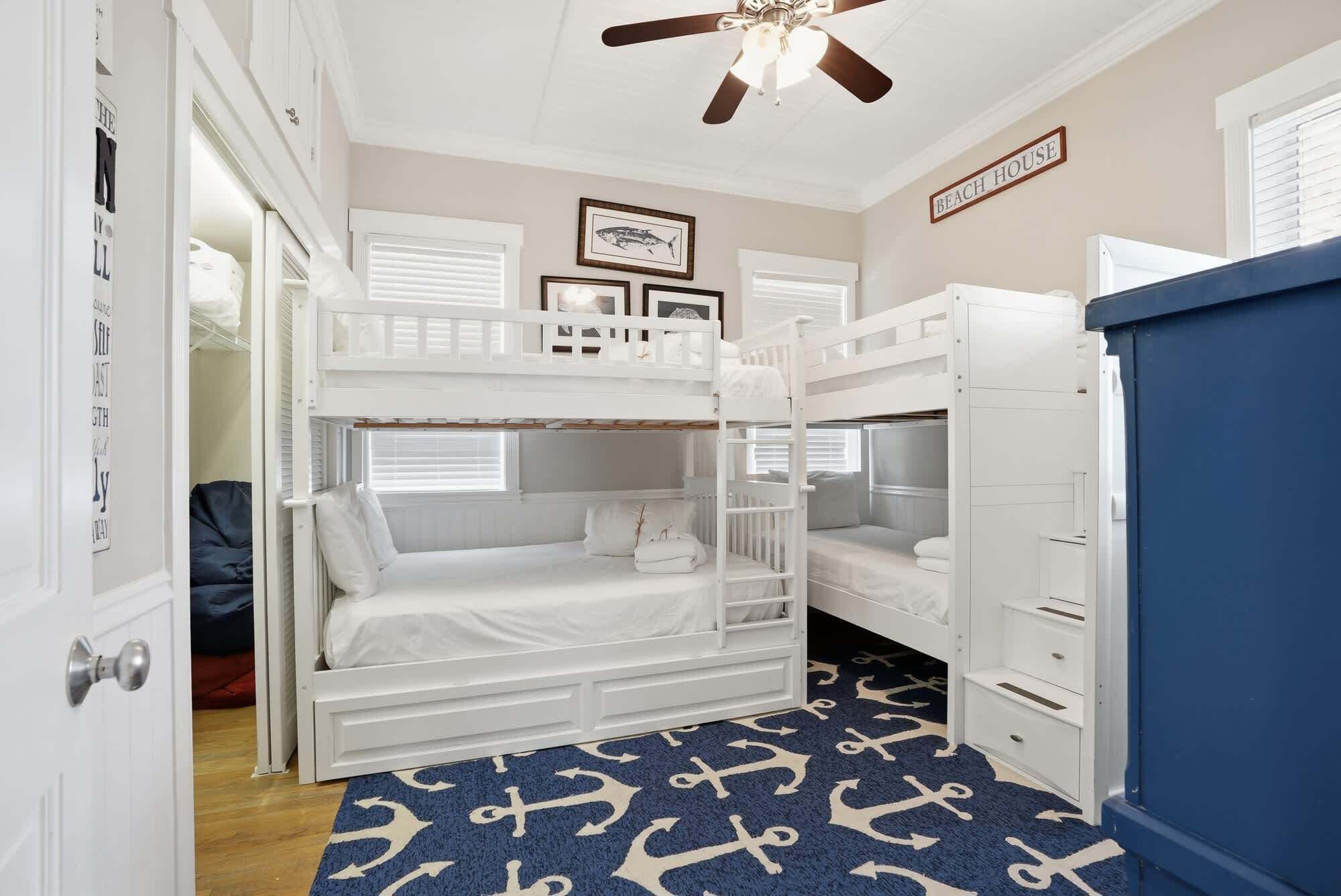 A bunk room with a ceiling fan, bunk beds, a dresser, and a rug with anchor patterns.