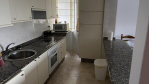 A compact kitchen with white cabinets, a microwave, a stove, and a sink. - Langosteira Apartaments (Fisterra)