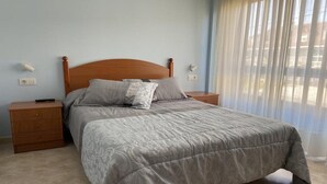 A bedroom with a wooden headboard, a grey bedspread, and a nightstand with a drawer. - Langosteira Apartaments (Fisterra)