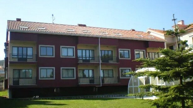A multi-story residential building with balconies and a green lawn in the foreground. - Langosteira Apartaments (Fisterra)