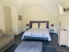 A bedroom with a bed, a sofa, a nightstand, a dresser, and a ceiling fan. - Gîte in Ardèche with swimming pool and magnificent view of the valley (Rochessauve)