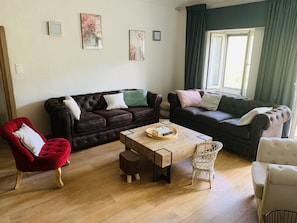 Un salon avec deux canapés de couleur marron foncé, une table basse en bois, un fauteuil rouge et une chaise en osier.