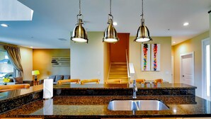 Cocina moderna con encimeras de granito, pileta de acero inoxidable y muebles de madera. Hay tres lámparas colgantes sobre la encimera.