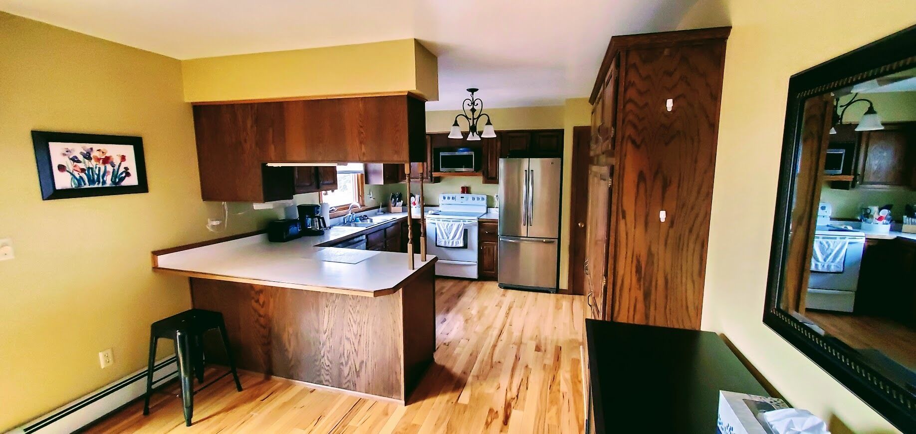 Une cuisine dotée de meubles en bois, d’un îlot central, d’un réfrigérateur et d’un coin repas visible à travers une porte ouverte.