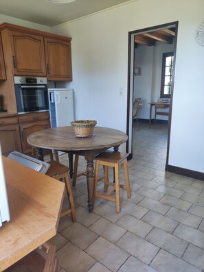 A kitchen with wooden cabinets, a round wooden table with two stools, and a refrigerator. - Grande Maison Familiale (Trélissac)