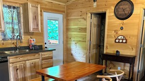 A wooden interior with a kitchen area featuring a wooden table and chairs, a sink, and a clock on the wall.