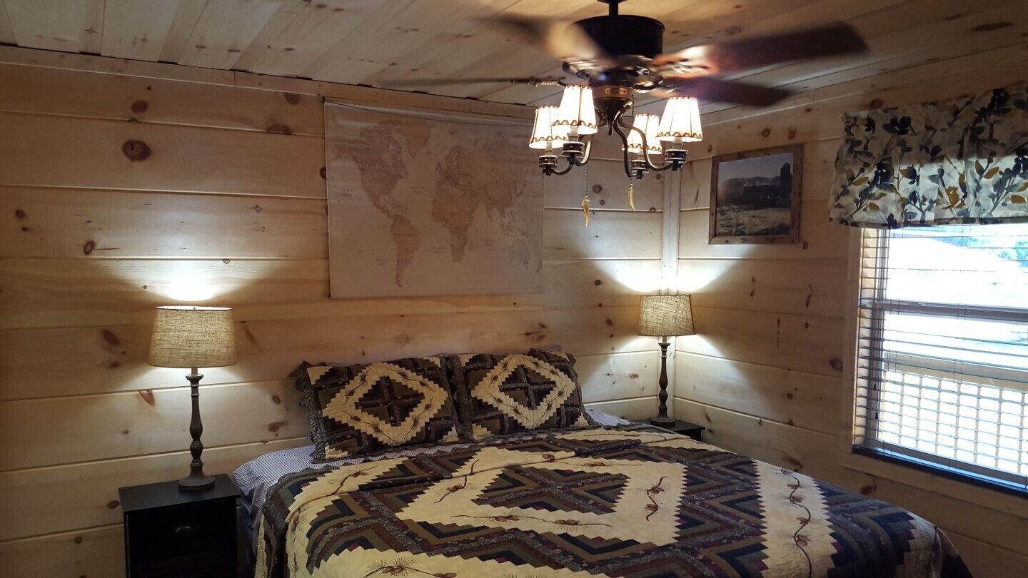 A cozy room with a wooden ceiling, a bed with patterned bedding, two wall-mounted lamps, and a world map on the wall.
